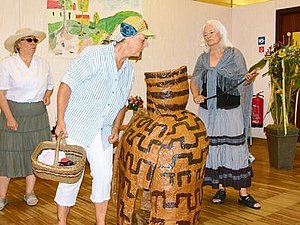 3 Schauspieler in verschiedenen Kostümen stehen mit einem großen Krug auf der Bühne.