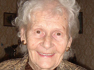Eine ältere Dame mit Dauerwelle lächelt fröhlich in die Kamera