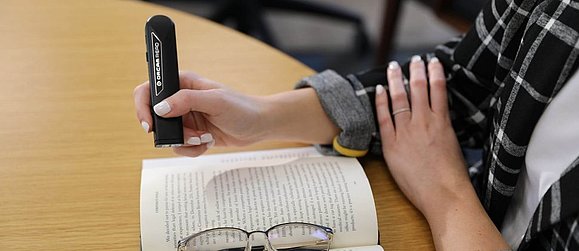 Person bedient schwarzes Gerät, das aussieht wie Laserpointer über einem Buch