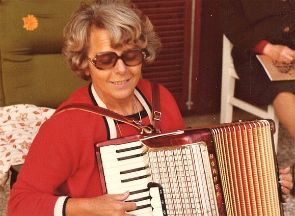 Wir sagen Bye Bye zu unserer lieben Frau Vater, einem kritischen und wachen Geist. Frau mit großen runden Brillen spielt Ziehharmonika