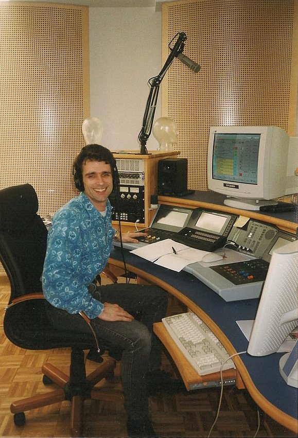 junger Mann sitzt am PC in Radiostudio der 80er mit Kopfhörern und blauem Hemd