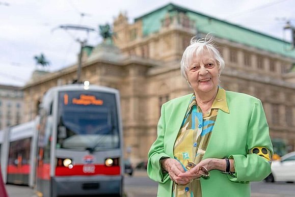 Frau J. vor der Staatsoper, im Hintergrund ist eine Straßenbahn zu sehen.