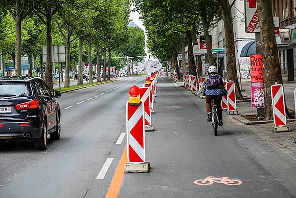 Eine dreispurige Straße ist geteilt durch Trennelemente. 2 Spuren sind für Autofahrer, 1 Spur ist für Radfahrer.