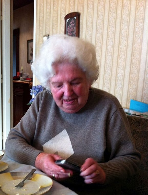 Eine ältere Dame mit weißer Dauerwelle blickt während des Sprechens auf etwas in ihrer Hand (verschwommen)