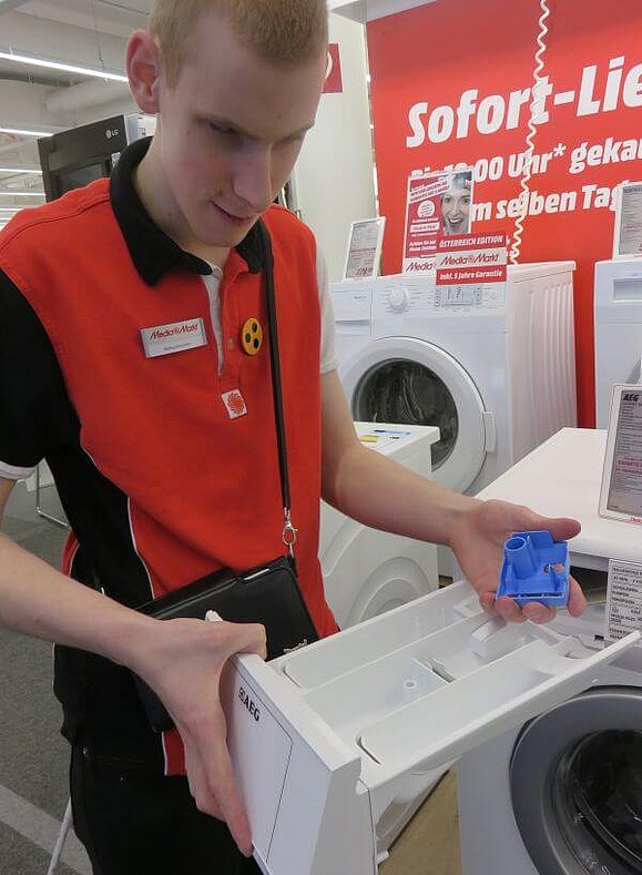Junger Mann hat Waschmitteleinlass einer Waschmaschine geöffnet