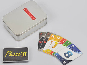 Eine Metallbox mit Braille-Schrift, eine Karte mit dem Phase 10 Logo und mehrere farbige Zahlenkarten mit Prägung liegen am Tisch.