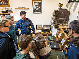 Polizist in Uniform zeigt Gruppe alte Enigma-Chiffriermaschinen.