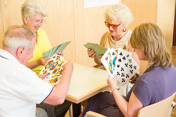 4 Personen mit großen Spielkarten in der Hand sitzen rund um einen Tisch.