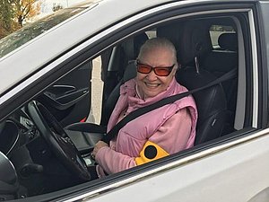 Seniorin in rosa Weste und Pullover sitzt angeschnallt in einem weißen Auto