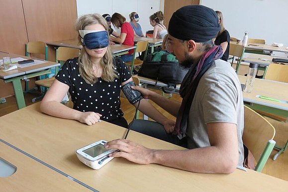 Schüler misst Blutdruck bei einer Schülerin mit Augenbinde
