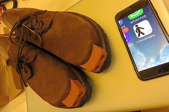 Braune Herrenschnürrschuhe mit Applikation vorne, daneben ein Smartphone mit der App Innomake.