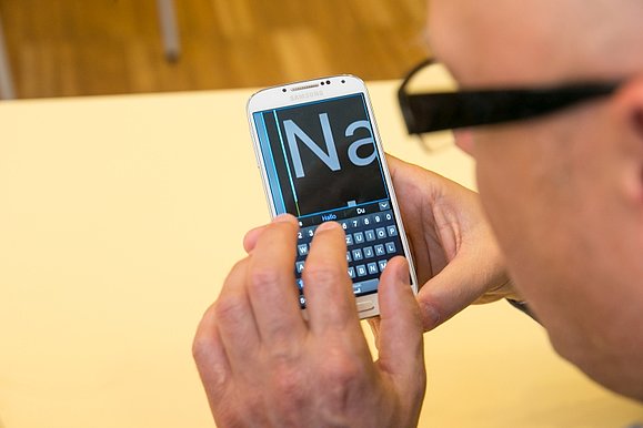 Ein Mann mit Brille bedient ein Smartphone. Am Handy sieht man den Inhalt in großer Schrift.