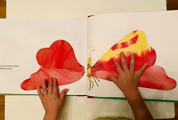 Zwei Kinderhände tasten einen bunten Schmetterling ab.