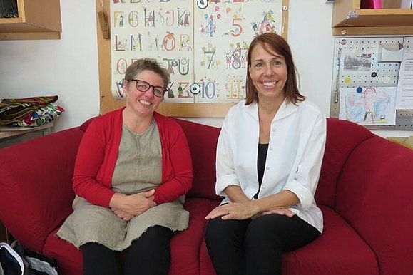 Direktorin Karin Feller und Sonderpädagogin Martina Mazal sitzen lächelnd auf einem roten Sofa