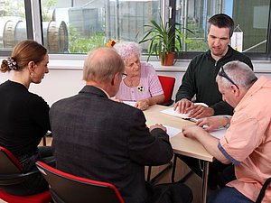 Mehrere Menschen sitzen am Tisch und berühren mit Händen Blatt mit Brailleschrift