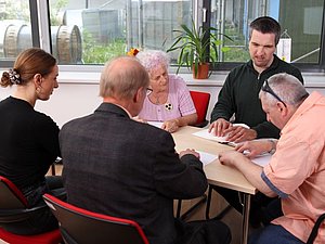 Mehrere Menschen sitzen am Tisch und berühren mit Händen Blatt mit Brailleschrift