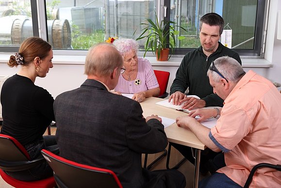 Mehrere Menschen sitzen am Tisch und berühren mit Händen Blatt mit Brailleschrift