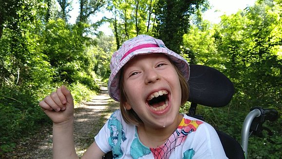 Anna lachend Die mehrfach behinderte Anna sitzt in ihrem Rollstuhl im Grünen und freut sich mit einem breiten, ansteckendem Lächeln