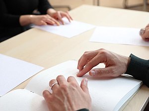 mehrere Hände lesen Brailleschrift am Tisch