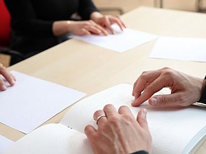 mehrere Hände lesen Brailleschrift am Tisch