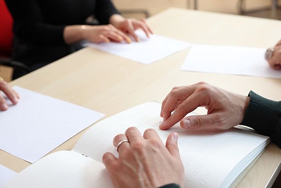 mehrere Hände lesen Brailleschrift am Tisch