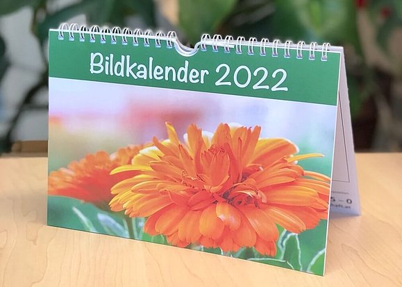 Ein Stehkalender mit Blumenmotiv und Aufschrift "Bildkalender 2022" auf der Vorderseite steht auf einem Tisch.