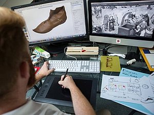 Mann sitzt vor 2 Bildschirmen und Tastatur, in seiner Hand ein Stift für den Computer, Copyright: Tactile Studio Paris