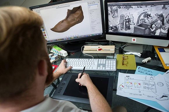 Mann sitzt vor 2 Bildschirmen und Tastatur, in seiner Hand ein Stift für den Computer, Copyright: Tactile Studio Paris