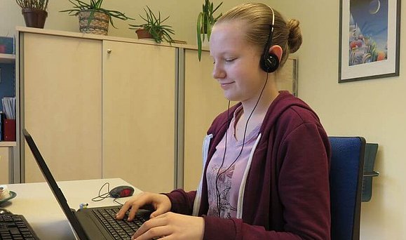 Eine junge Dame mit Kopfhörern sitzt vor einem Laptop und arbeitet