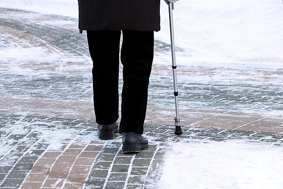 ältere Person von hinten mit Gehstock auf Schneeboden