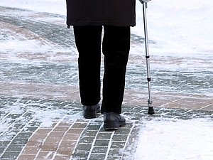 ältere Person von hinten mit Gehstock auf Schneeboden