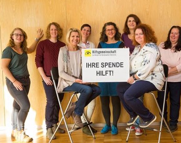 Mitarbeiterinnen der Hilfsgemeinschaft halten lächelnd ein Schild mit dem Wort "Danke!" in die Kamera.