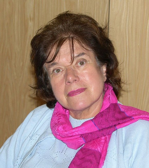 Frau mit dunkelbraunen Haaren bis zur Schulter, hellblauem Pullover und pinkem Schal