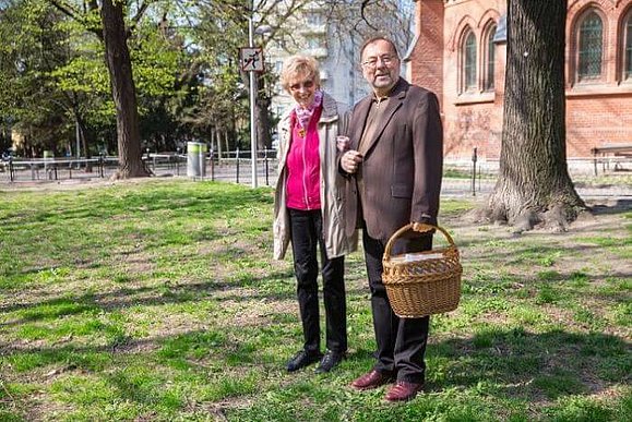 Heinz Tichy steht mit einer sehbeeinträchtigten Frau in einem Park, er hält einen braunen Korb.
