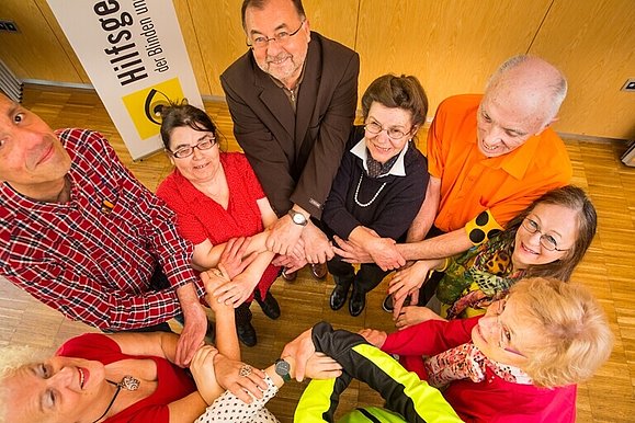 Mitglieder der Hilfsgemeinschaft und Freiwillige bilden einen Kreis indem sie die Hände ineinander verschränken