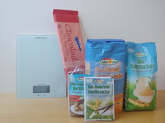Wir verlosen diese sprechende Waage und hochwertige Backzutaten für einen Schokokuchen Küchenwaage mit Backzutaten wie Mehl, Schoko und Zucker