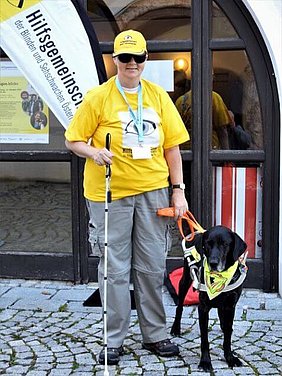 Eine Frau mit Taststock und Blindenhund.