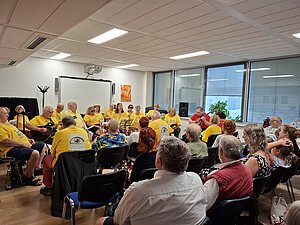 Die Singgruppe Kunterbunt beim Sommerkonzert
Foto: © Hilfsgemeinschaft Gäste sitzen in einem Saal und hören der Singgruppe beim Musizieren zu