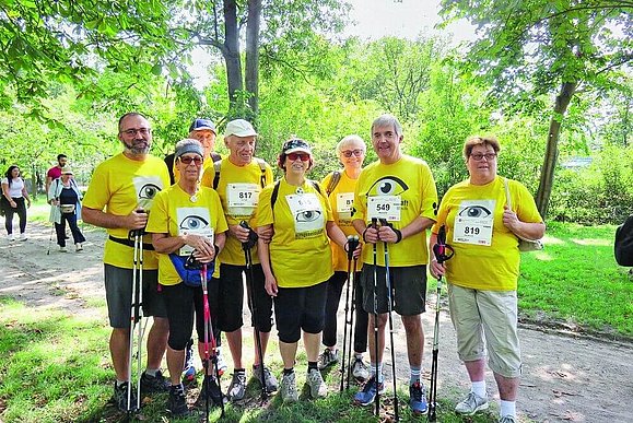 Gruppe von Menschen im Wald mit Nordic Walking Stöcken und gelben T-Shirts.