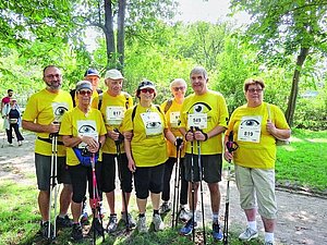 Gruppe von Menschen im Wald mit Nordic Walking Stöcken und gelben T-Shirts.