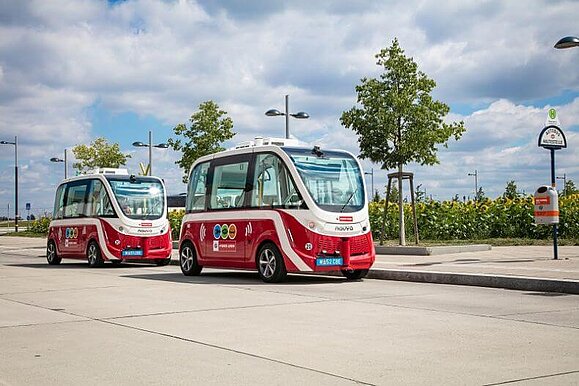 Zwei Rot-weiße E-Busse stehen im Freien, im Hintergrund der Himmel und Bäume