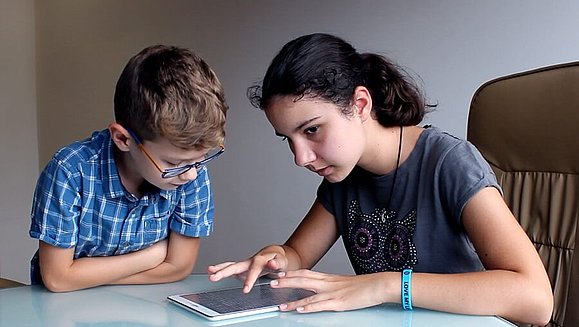 Maks sitzt mit seiner blinden Schwester Mia vor dem Tablet, Mia führt ihren Zeigenfinger über das Tablet , Copyright: Feelif