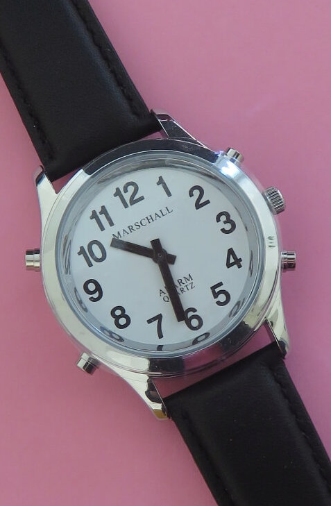 Sprechende Uhr mit silberfarbenem Uhrengehäuse, kontrastreichem Ziffernblatt und schwarzem Lederband.