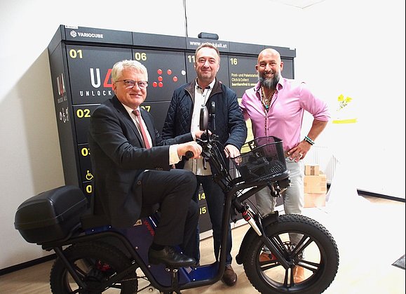 Drei Herren mit schwarzem E-Lastenbike vor Paketbox