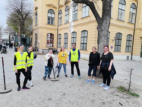 mehrere Menschen stehen unter Baum, teils mit Warnwesten und gelber Armbinde