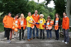 9 Personen in orangen und gelben Shirt hinter der Startlinie der Wanderung, Copyright: World Vision Österreich.