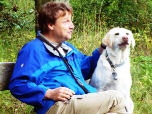 Per Busch sitzt auf einer Parkbank mit Hund Peggy