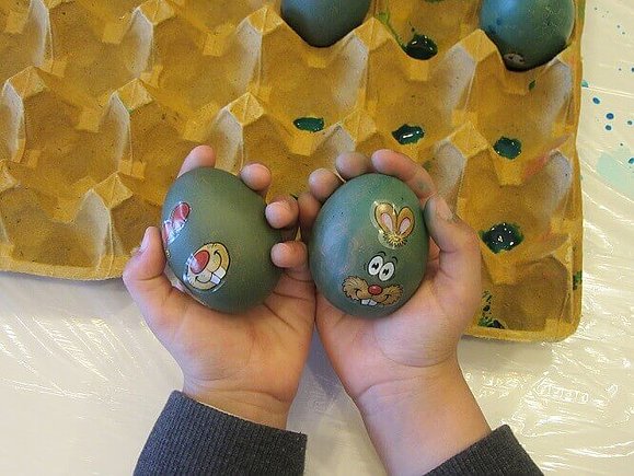 Kind hält zwei grün gefärbte Eier mit Hasen-Stickern in den Händen.