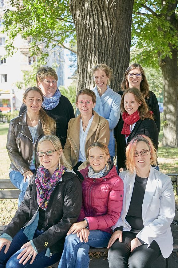 9 Frauen posieren lächelnd für ein Gruppenfoto im Freien.