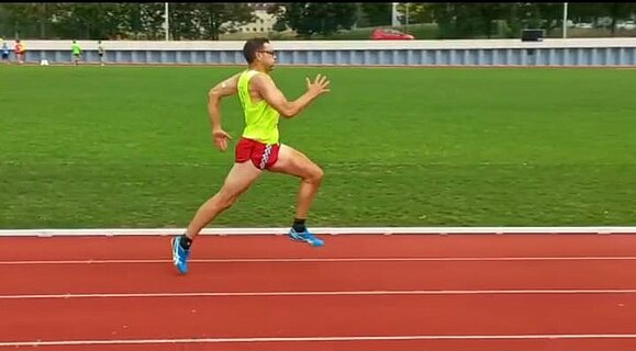 Mann mit gelbem Shirt und roter Hose sprintet über roten Boden